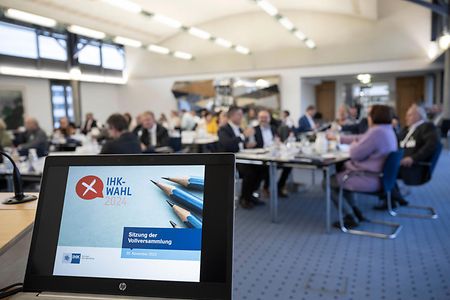 Bildschirm mit Päsentation, im Hintergrund Gespräche an Tischen
